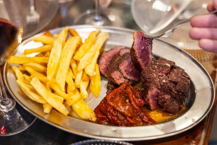 Una bandeja de metal con solomillo, pimientos rojos y patatas fritas.