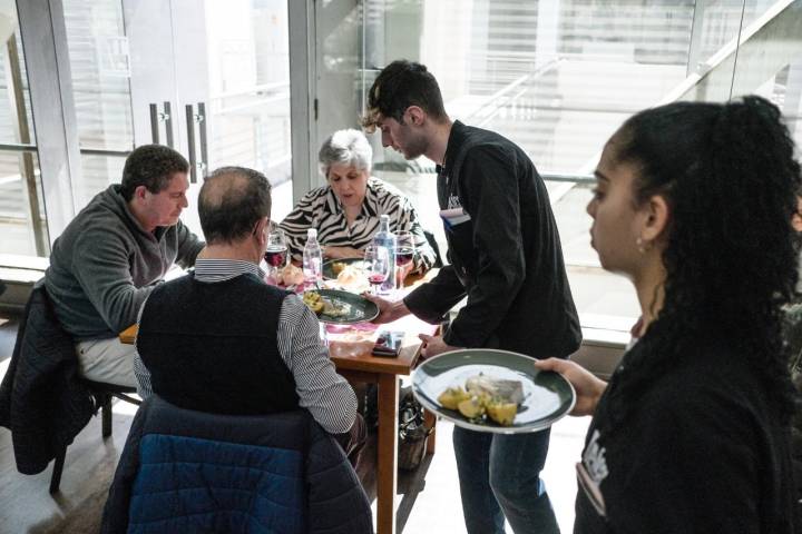 Una mesa con tres comensales es atendida por uno de los alumnos de la escuela.