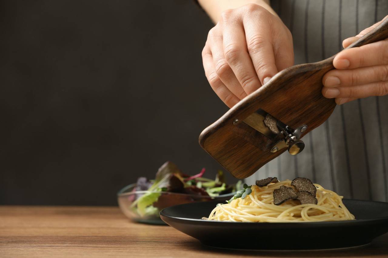 Una mujer rayando trufa en un plato de pasta