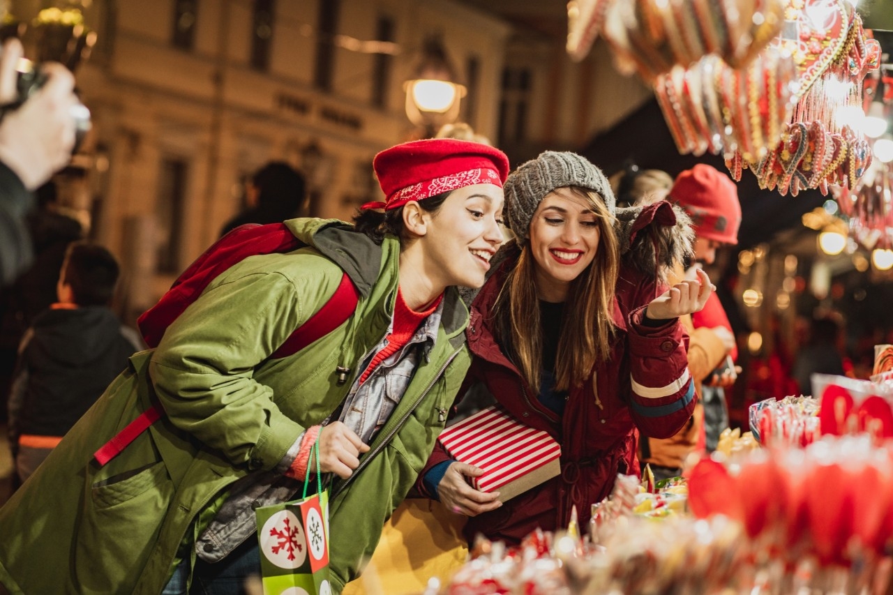 Two female friends are outdoors during winter and shopping on the Christmas market