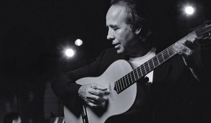 Una foto de Serrat tocan la guitarra en concierto.