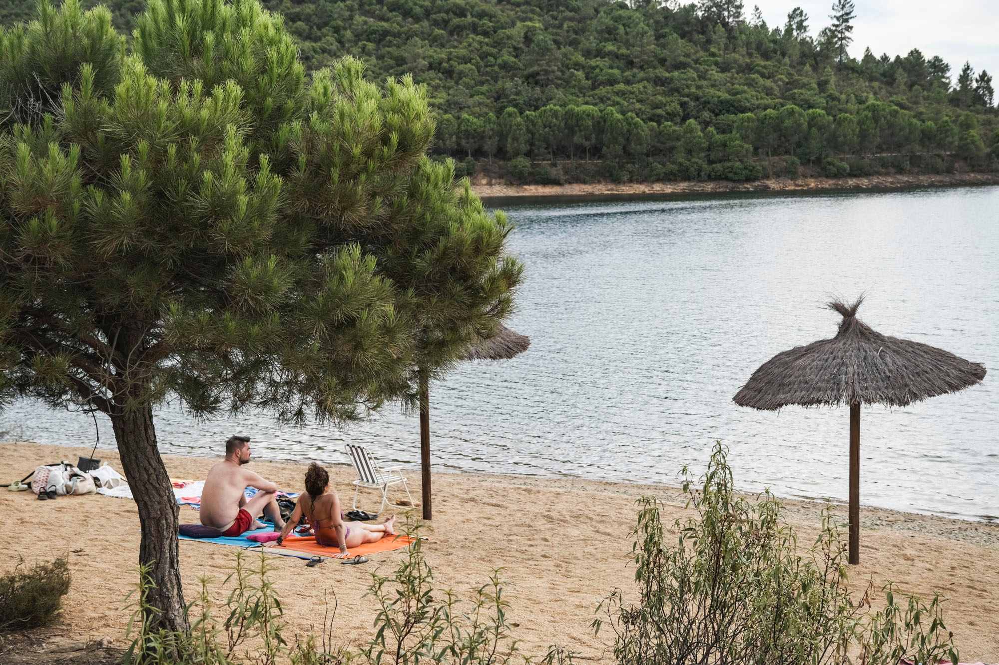 Un pareja toma el sol en la playa con el agua al fondo.