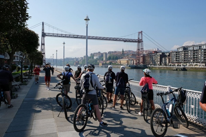 Un grupo de ciclistas observan el Puente Colgante cerca del monumento a Evaristo Churruca, en Getxo (Vizcaya).